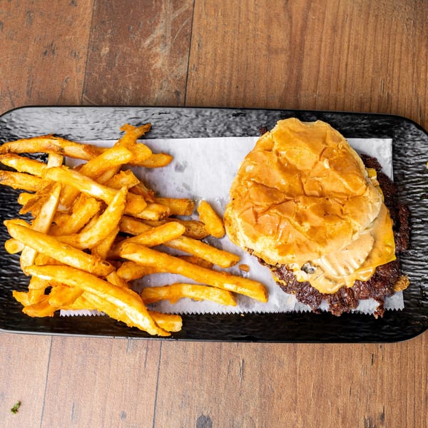 A black plate with a cheeseburger and a pile of golden french fries on a wooden table.